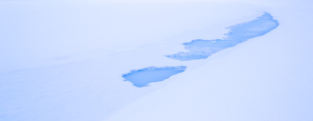 Blue thaw patches in ice and snow on a winter lake