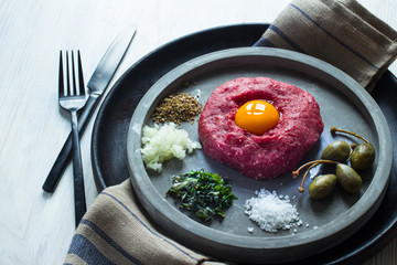 Beef Tartar mit Ei, Kapern, Zwiebeln, Salz auf einem modernem Teller mit Besteck