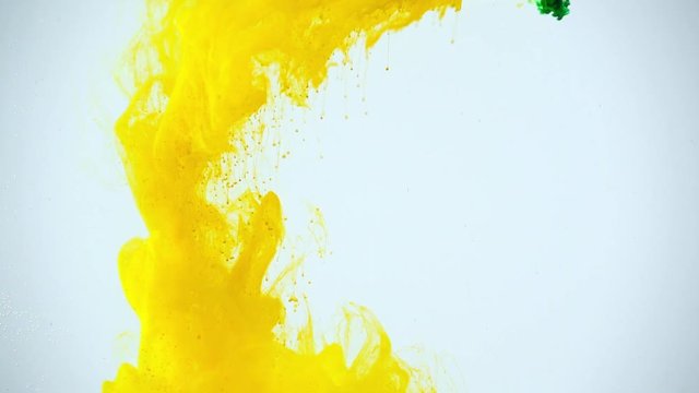 slow motion shoot of green and yellow paints dissolving in water on grey background