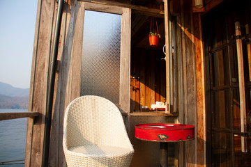 White weave chairs and red steel table with glass wooden window on terrace near the lake for relax at floating home stay.