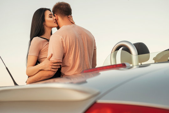 Gorgeous sexy copule of man and woman on a vacation car trip in summer day. Luxury grey sport car. Sexy fit brunette woman and man in casual outfit. Sunset
