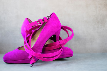 Bright pink high-heeled shoes and a pink belt on gray background.