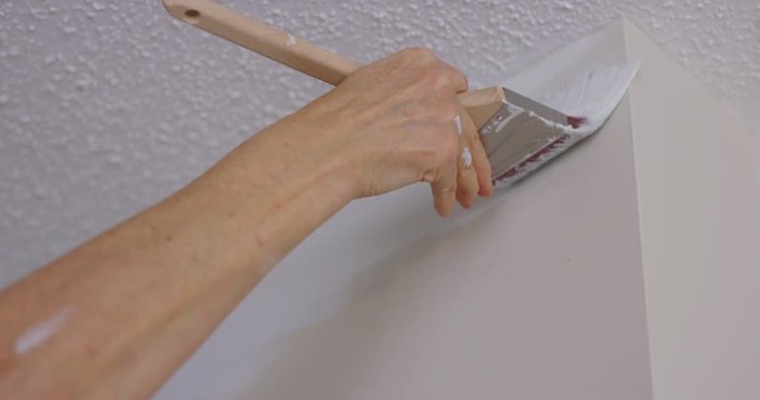 Woman painting edge of ceiling - close up on paint brush