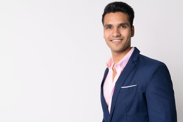 Profile view of young happy Indian businessman in suit looking at camera