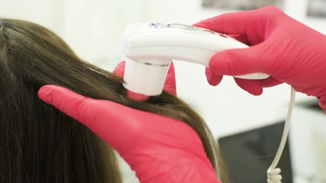 doctor dermatologist diagnoses the structure of the hair of a young pretty girl with a special tool - a trichoscope. Trichology, trichogram