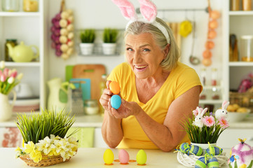 Happy senior woman decorating Easter eggs to holiday