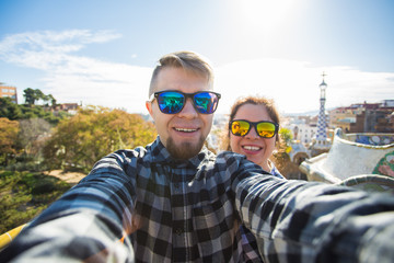 Funny young couple looking at camera taking photo with smart phone smiling in Park Guell,...