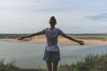 The woman stands back with open arms. The view of river and hill.