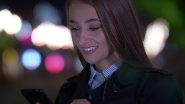 Fullface shot of Caucasian businesswoman standing on the street, reading and texting messages on smartphone and smiling