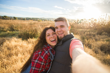 Travel, vacation and holiday concept - Happy couple having fun taking selfie against background on the field and sunset