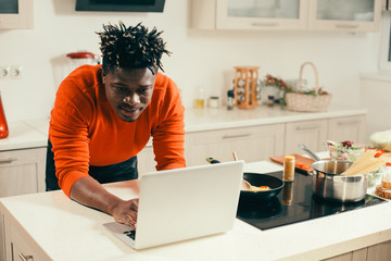 Attentive young man using modern laptop in the kitchen