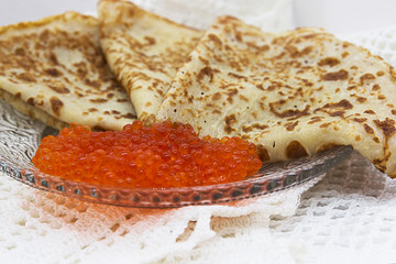 Traditional Russian pancakes with red caviar on a glass plate