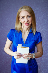 A woman in a blue dress on a purple background holding a white notebook