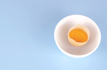 Broken egg with yolk and protein in a deep white plate.