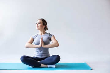Fototapeta premium Bawi się kobiety w lotosowej pozyci na błękitnej joga macie na szarym tle.