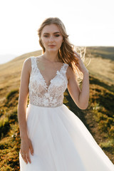 Fototapeta na wymiar Stylish bride standing on beautiful landscape of mountains on sunset