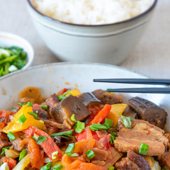 Fried pork with eggplants and sweet peppers in a large bowl and a cup of rice - a traditional Asian dish