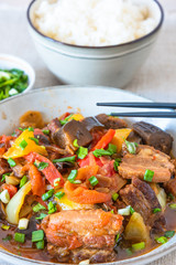 Fried pork with eggplants and sweet peppers in a large bowl and a cup of rice - a traditional Asian dish