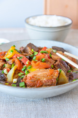 Fried pork with eggplants and sweet peppers in a large bowl and a cup of rice - a traditional Asian dish
