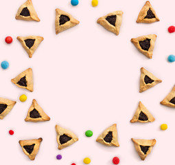 Triangular cookies with poppy seeds ( hamantasch or aman ears ), colored candy for jewish holiday of purim celebration on pink background with space for text. Top view, flat lay