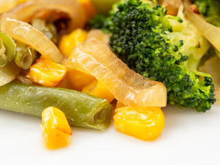 cooked vegetables broccoli, carrots, green beans, corn on a white plate. macro