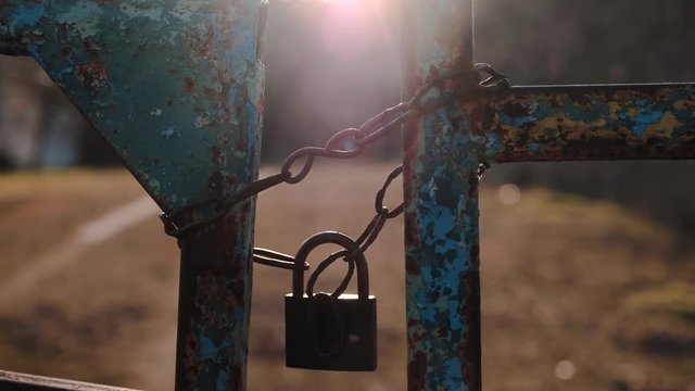 The sun's rays illuminate the old rusty lock on the chain, which closed the entrance gate