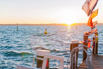 Sunset with red-yellow sun on a lake or sea. Sky, shore, sun and water. Flags of different cities,...
