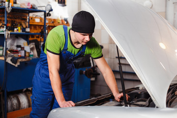 A young man repairs a car in his garage.