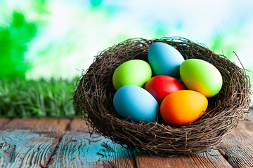 Colored Easter eggs in the nest on wooden table and nature background