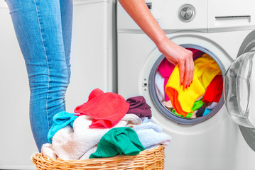 Young woman loads the laundry in the washing machine from the laundry basket before washing.
