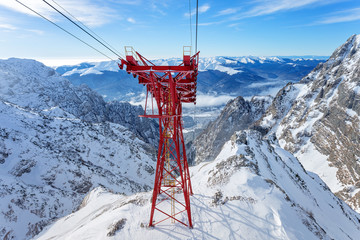 Red Cable Car Pylon and cables way at mountains landscape. Blue sky and massive mountains in...