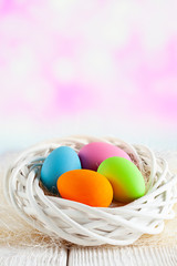 Four Easter eggs in white nest on table and pink abstract background