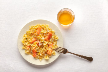 Smoked salmon with bowtie pasta. Farfalle with salmon and a cream sauce, shot from the top on a white linen tablecloth with a fork, a glass of wine, and copy space