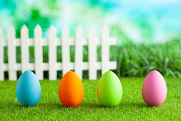 Easter eggs on grass, white fence on nature background