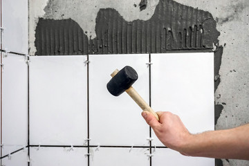 The worker's hand is putting tiles adhesive to the wall with the notched trowel.