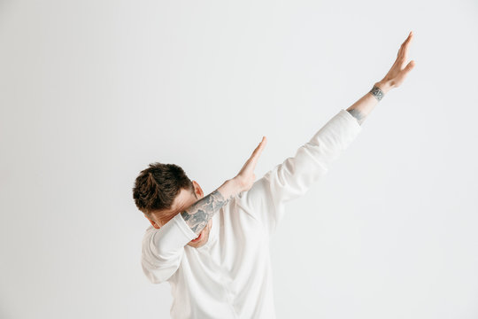 Young man makes a dab movement with his arms on a gray background. Human emotions, facial expression concept