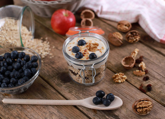 light healthy breakfast  with yogurt on oatmeal muesli , blueberries and walnuts in a glas on a rustic wooden table