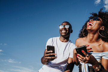 Two happy friends using the mobile in the street. Friendship concept.