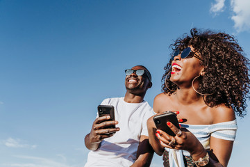 Two happy friends using the mobile in the street. Friendship concept.