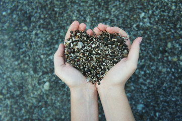 Hands full of small stones in a heart shape on a stony beach of Crete, Greece. Lifestyle concept. Love and romance sign.  
