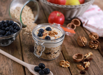 light healthy breakfast  with yogurt on oatmeal muesli , blueberries and walnuts in a glas on a rustic wooden table