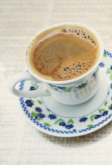 A tiny cup of Turkish coffee with a rich foam in a cafe, close-up. Served in a nice cup with pretty blue flowers. 
