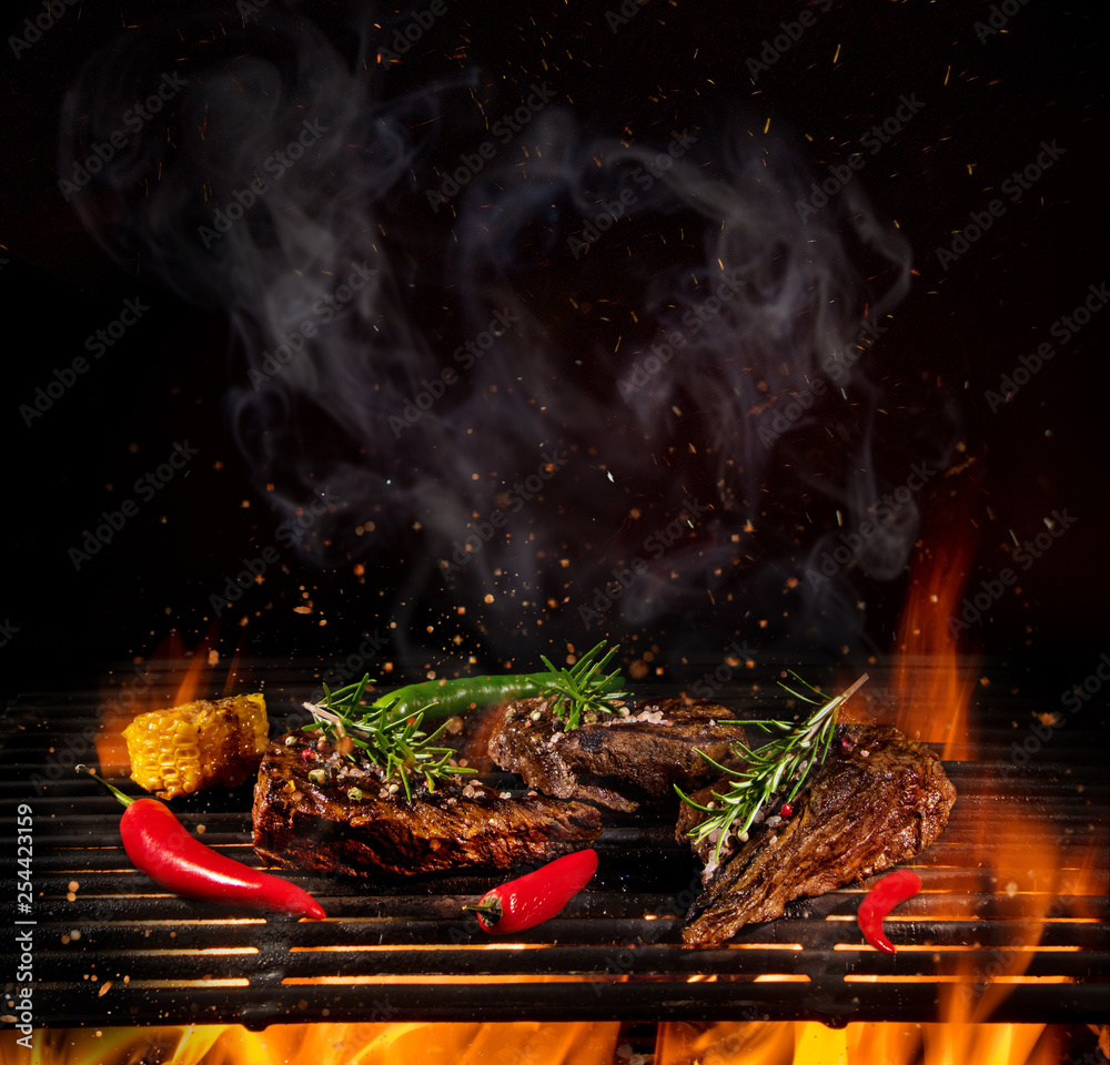 Wall mural Tasty Beef steaks on iron cast grate with fire flames.