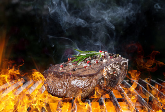 Tasty Beef steaks on iron cast grate with fire flames.