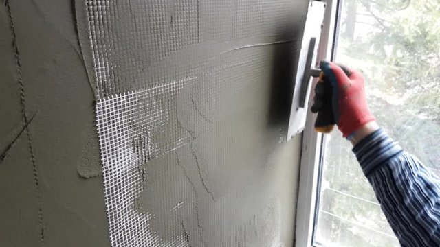 Forming of smooth hard surface on interior walls of apartment. Repairman plastering wall with putty knife