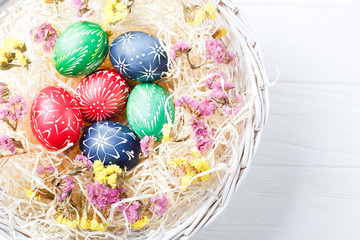 Hand painted different colors easter eggs in nest and flowers on white wooden table with place for text