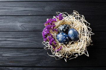 Hand painted dark blue easter eggs in nest and flowers on wooden table
