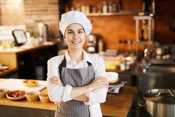 Waist up portrait of young cook smiling at camera while posing in restaurant kitchen, copy space