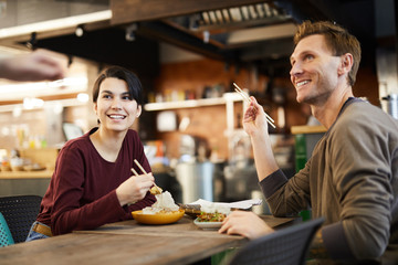 Portrait of cheerful young couple enjoying Asian food in restaurant, copy space