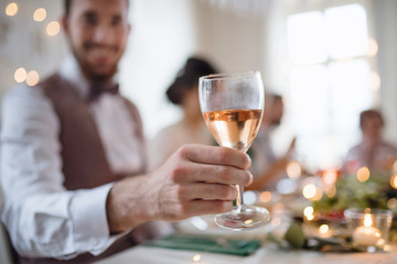 A close-up of male hand indoors in a room set for a party, holding a glass of wine.